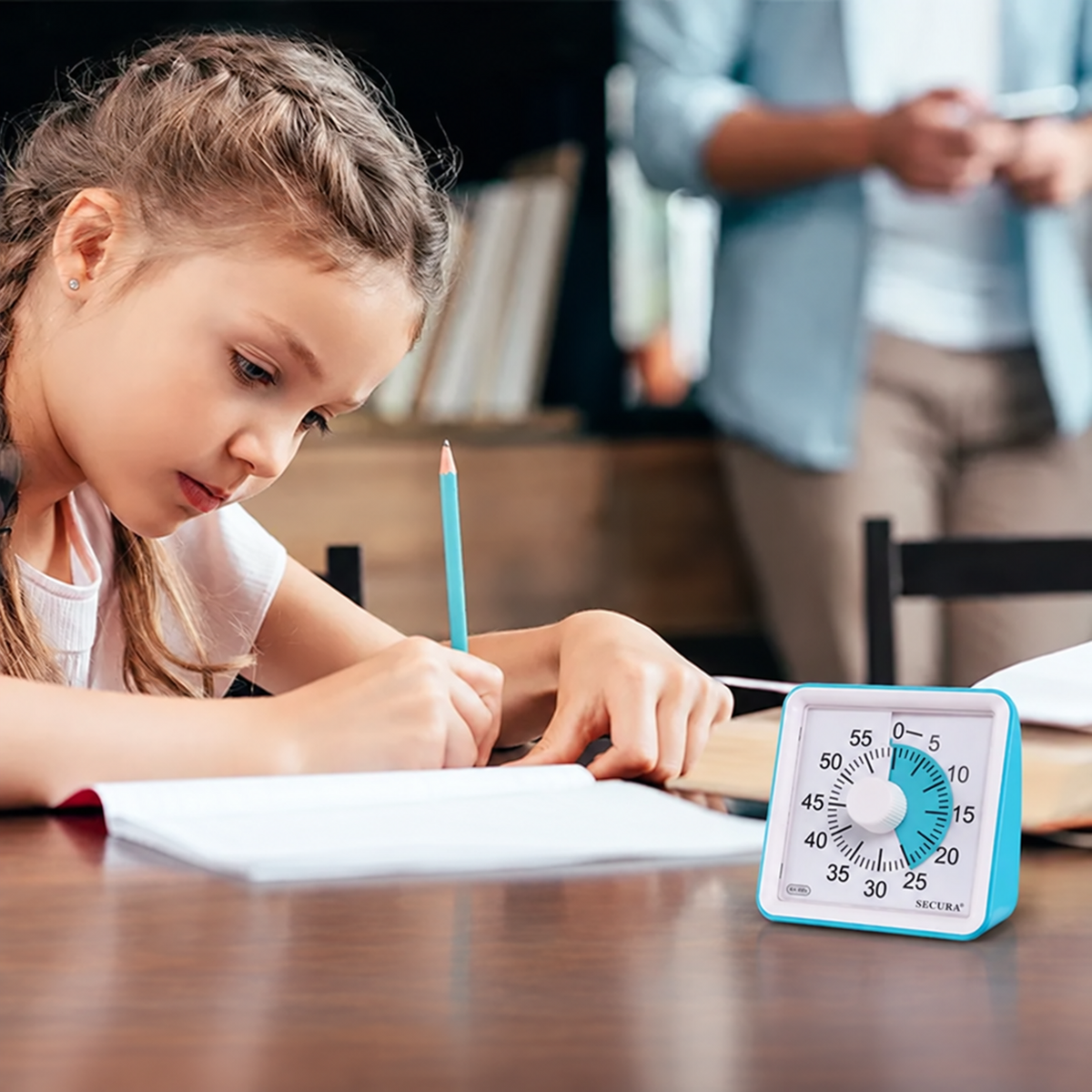 A student writing at a desk with the blue Secura visual timer beside her notebook.