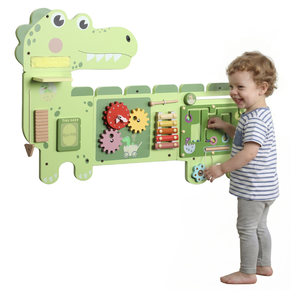 A child standing beside the green Qaba dinosaur wall busy board and exploring its sliding maze.